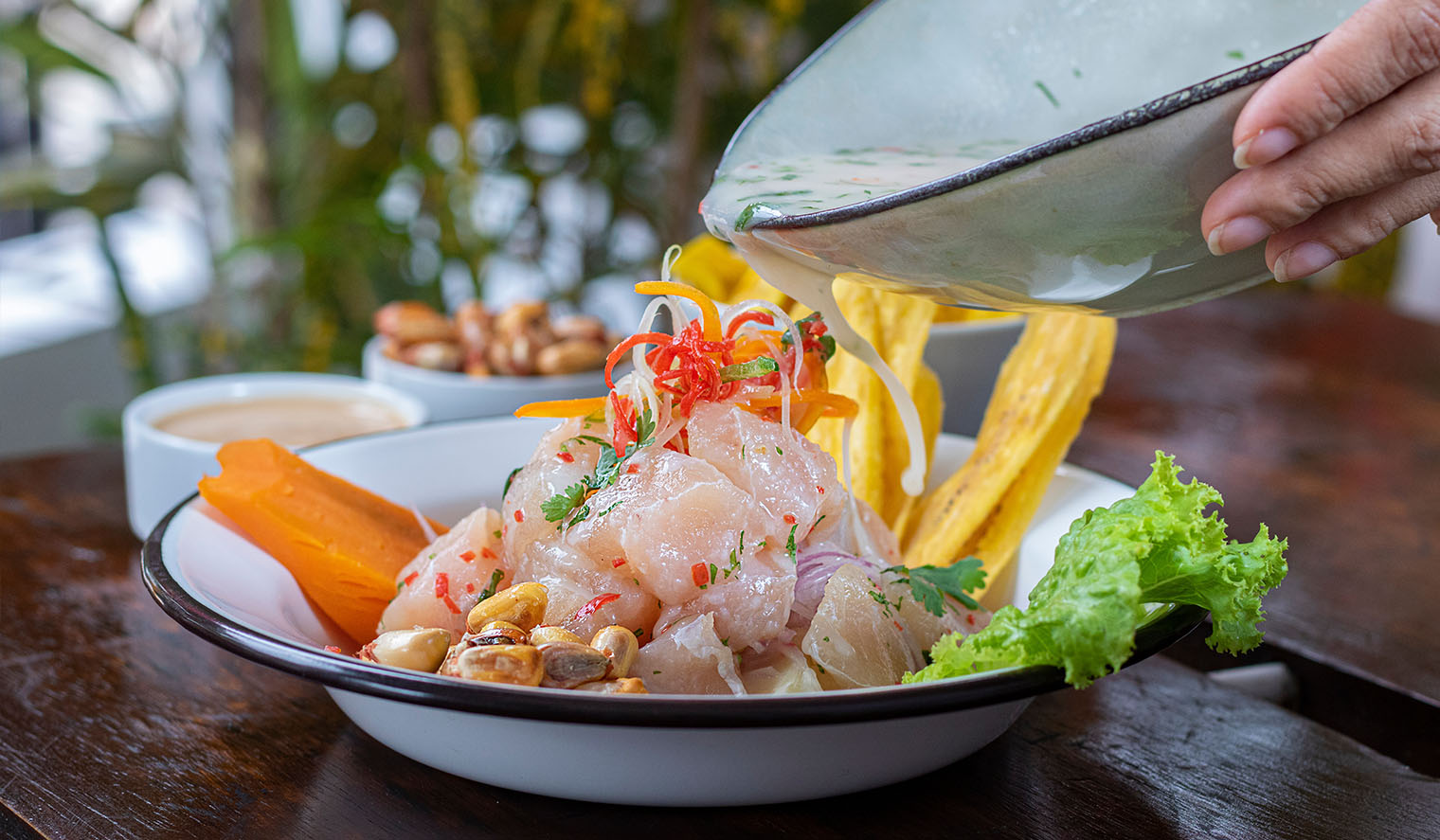 Frisch zubereitetes peruanisches Ceviche mit rohem Fisch, Zwiebeln, Chili und Koriander, serviert mit geröstetem Mais, Süsskartoffel, Kochbananenchips und grünem Salat in einem Restaurant in Cusco